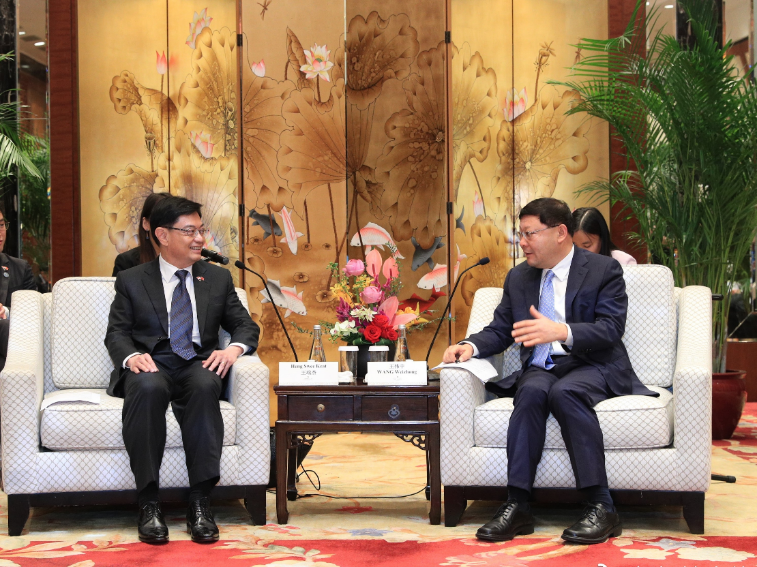 Two men in suits seated facing each other for a meeting, with decorative floral screen behind.